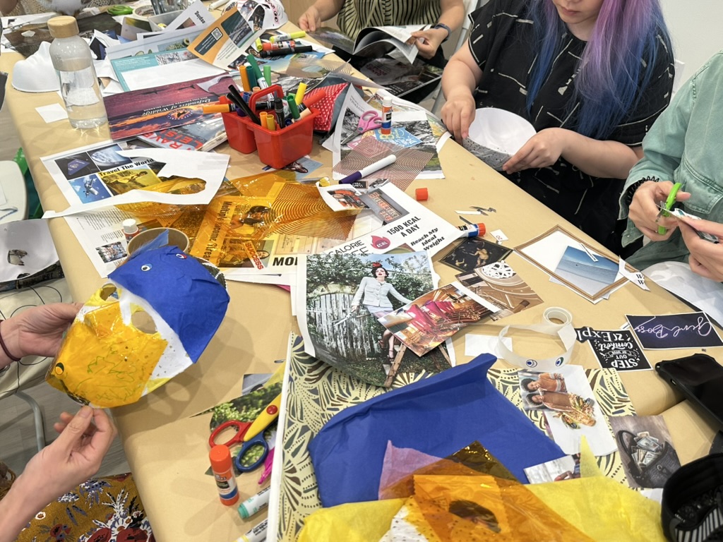 Mask collage materials and works in progress on a long table