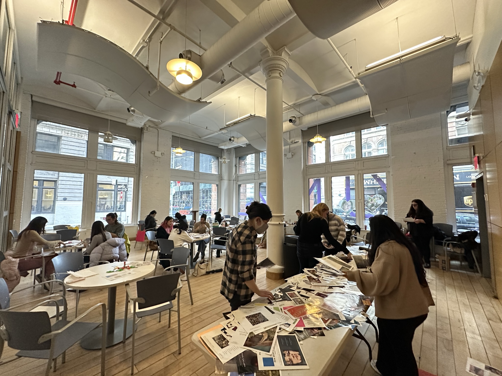 Large studio with participants gathered at tables sorting magazine clippings for a collage workshop